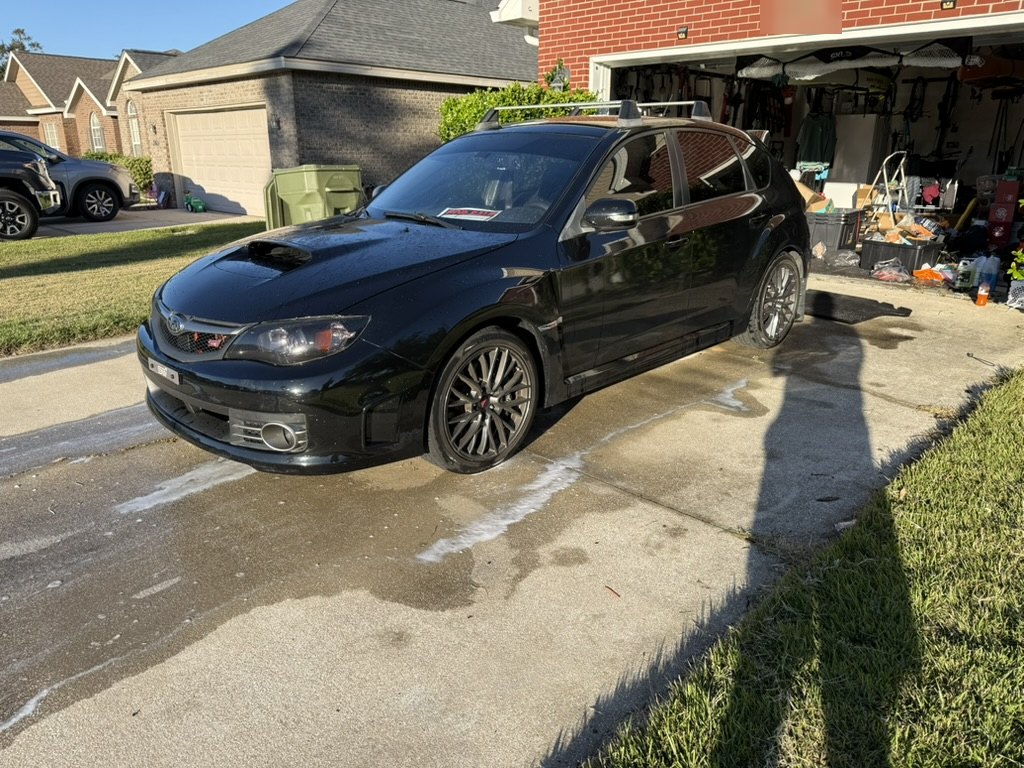 Black 2010 Subaru WRX STI hatchback, front three-quarter view with roof rack